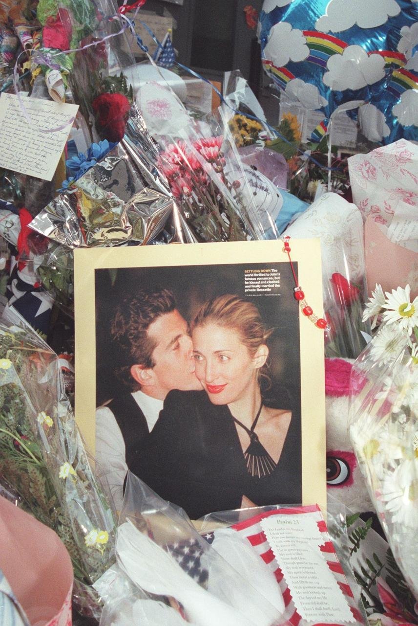 A photo of John F. Kennedy Jr and his wife Carolyn Bessette Kennedy is surrounded by balloons and flowers at a makeshift shrine in front of their apartment building in New York City 21 July 1999. The body of John F. Kennedy, Jr has been located and removed from the wreckage of the small plane he was flying with his wife Carolyn Bessette Kennedy and her sister Lauren G. Bessette on 16 July off the coast of Martha's Vineyard. (Photo credit should read HENNY RAY ABRAMS/AFP via Getty Images)